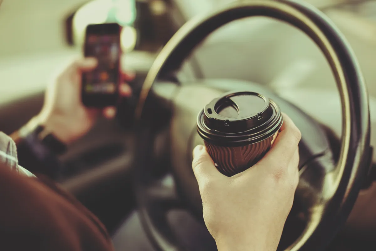 a driver texting and driving with one hand that's also gripping a coffee cup indicating reckless driving