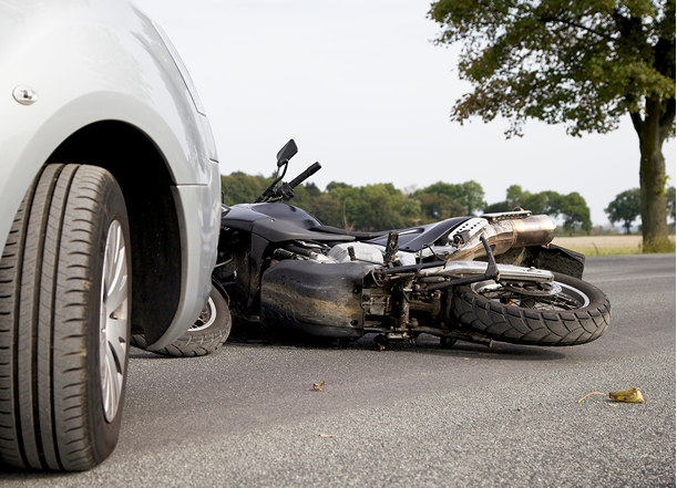 A damaged, burnt motorcycle lying on its side in the middle of a busy city intersection after a traffic accident.