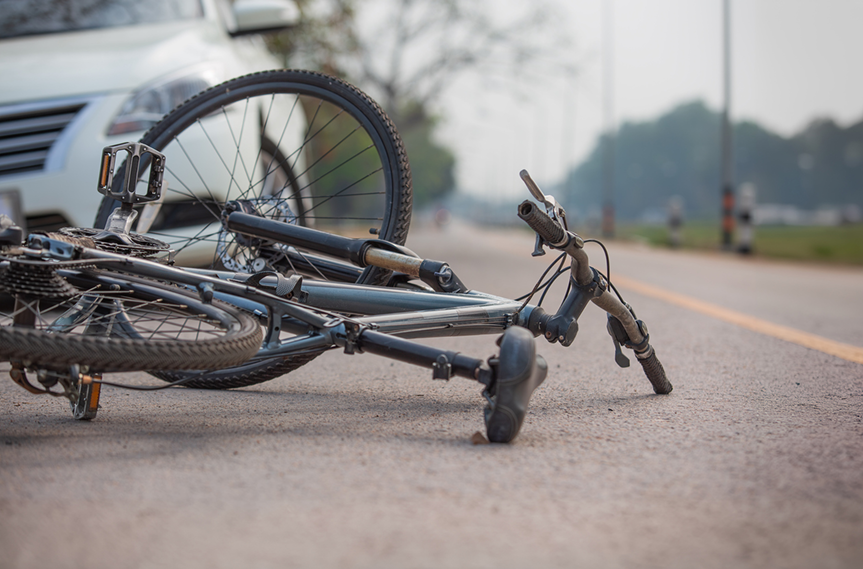 A bicicle is lying on the street in front of a car.